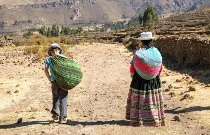 Peru itineraries - photo of a boy helping his host to carry goods in colourful sack