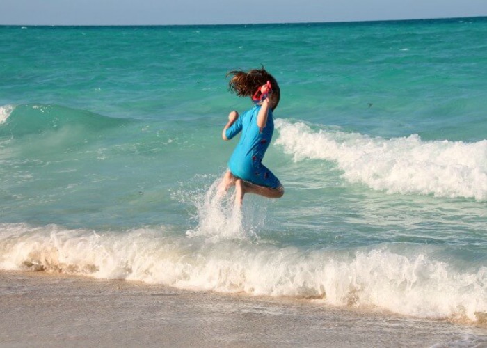 Girl jumping into an azure sea in Cuba on a long haul family holiday