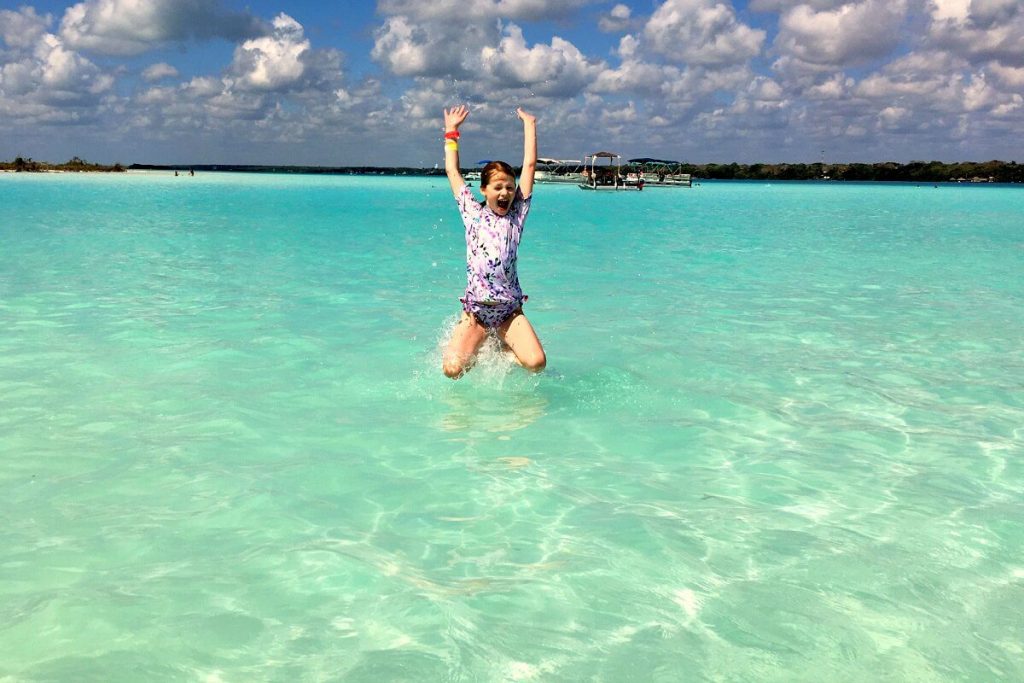 Best family beaches - photo of a young Stubborn Mule Travel customer jumping in an azure blue ocean