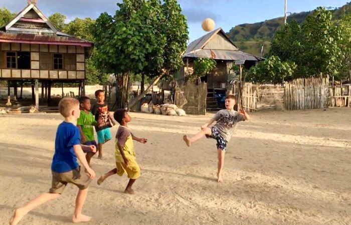 Local kids and young tourist playing football on beach in Bali on a Bali with kids holiday