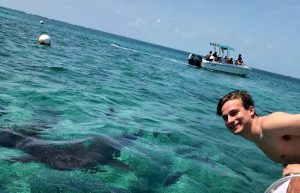 Young man learning out of boat to pose with benign shark in Belize