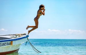 Best family beaches - young girl jumping into azure waters from a boat