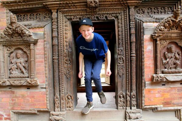 Nepal with kids itinerary - teenager stepping through ancient carved door frame