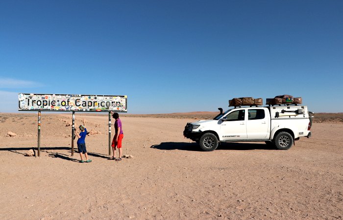 Namibia with kids self-drive itinerary - family with car beside Tropic of Capricorn sign