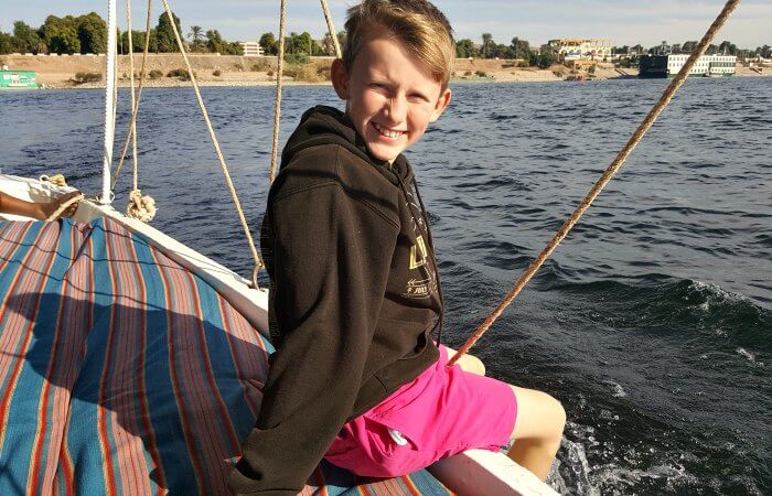 Child sitting on edge of boat as it sails along the Nile - family Christmas breaks