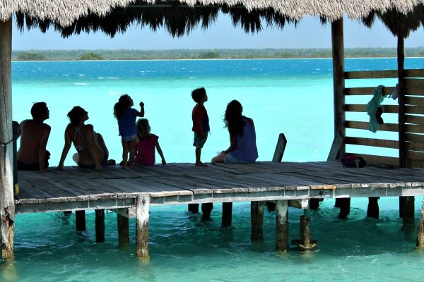 Family sitting on jetty on Lake Bacalar, Mexico - masthead for Easter family holidays