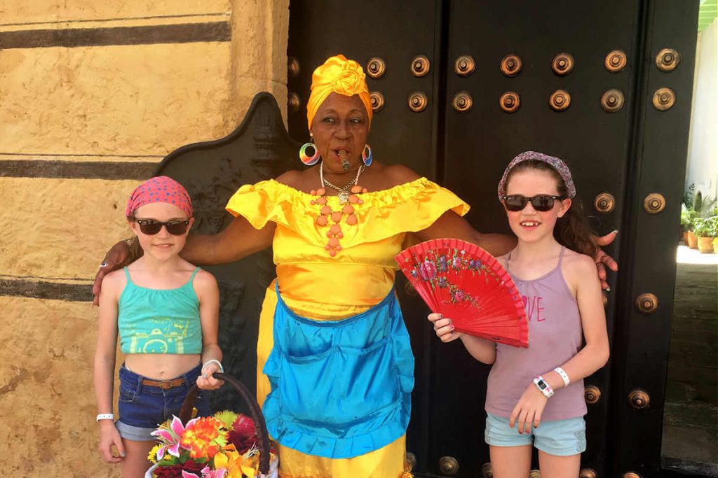 Cuba with kids masthead - young visitors with Cuban lady in bright coloured outfit