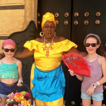 Cuba with kids masthead - young visitors with Cuban lady in bright coloured outfit
