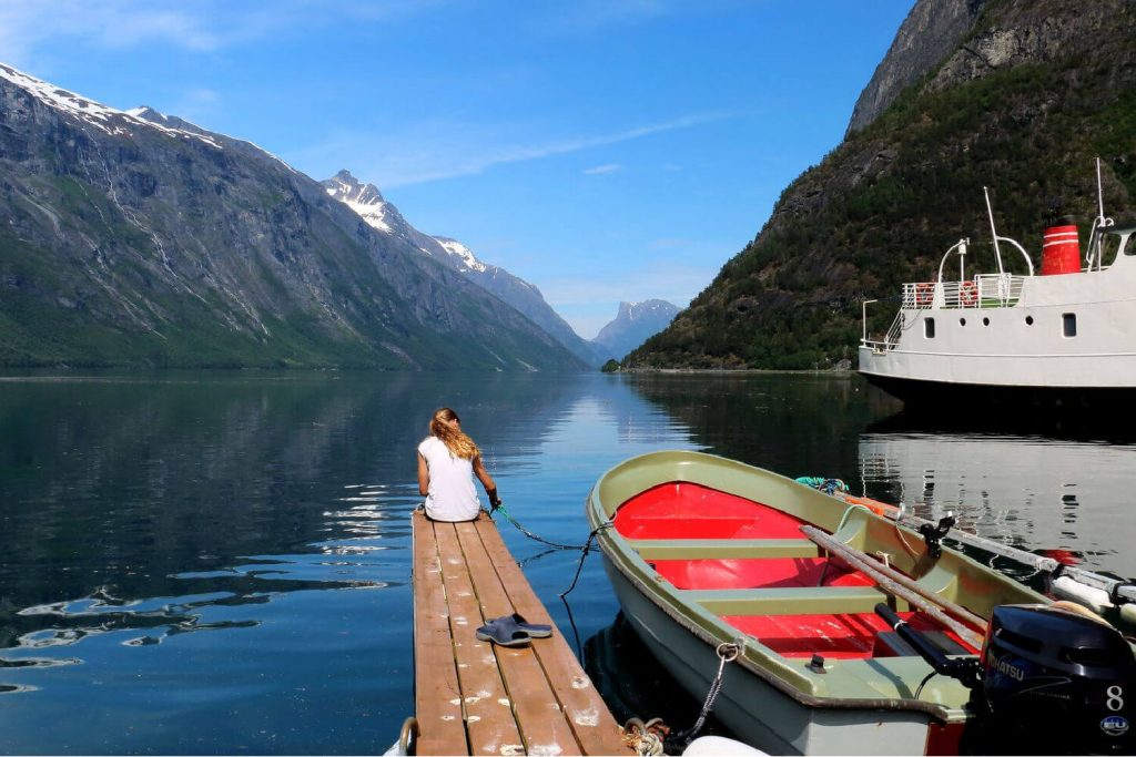 Norway family holidays, stunning view of fjord with young woman sitting on a dock looking into the distance