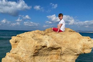 Crete family holidays - boy on beach rock with blue sky background
