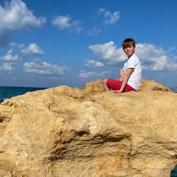 Crete family holidays - boy on beach rock with blue sky background