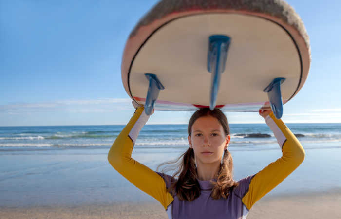 Teenager holding her surfboard above her head. in Portugal