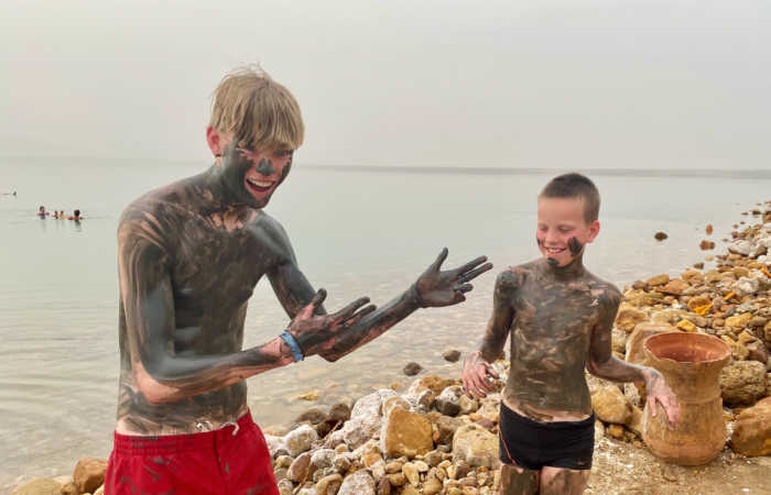 Teenager and little brother cover themselves in mineral mud at the Dead Sea - Jordan with kids holiday