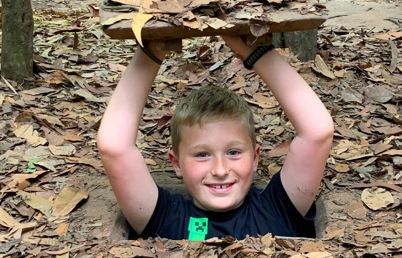 Boy exploring Cu Chi tunnels in Vietnam, showing camouflaged entrance hidden in leaves