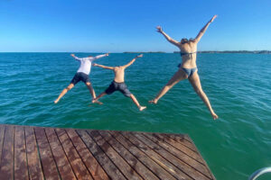 Three kids jumping off jetty into the blue ocean on Belize holiday with kids