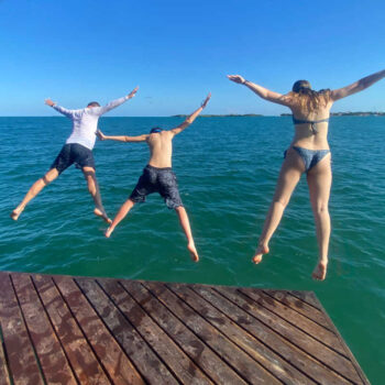 Family jumping off jetty into turquoise sea on Belize with kids holiday