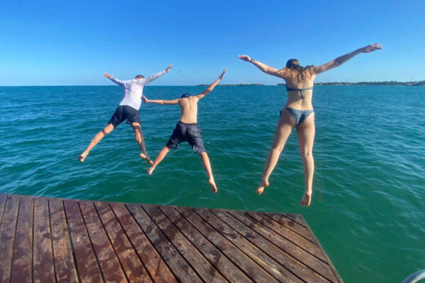 Family jumping off jetty into turquoise sea on Belize with kids holiday