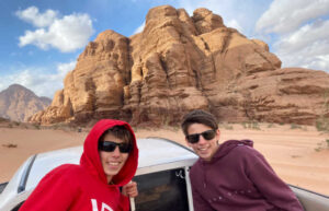 Family holiday, teens exploring Jordan's Wadi Rum by 4-wheel drive truck, with desert rock formation in the distance