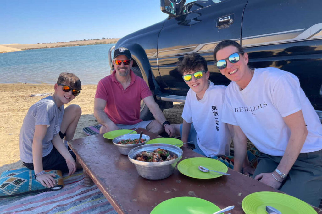 Family on Egypt day trip eating lunch in the shade of their vehicle - May half term holidays