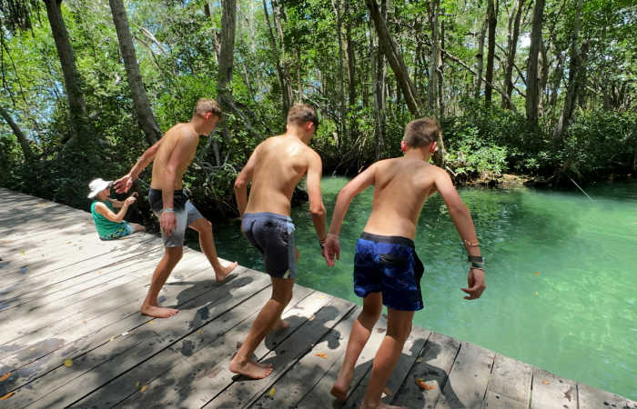Three teenagers jumping into a turquoise coloured water in a Mexican cenote on self-drive family road trip