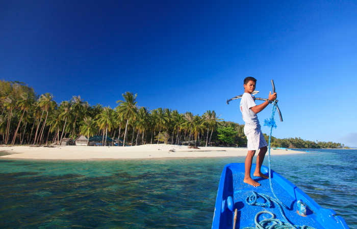 Best Asia family destinations, idyllic island in the Philippines, boy holding anchor on boat approaching an island