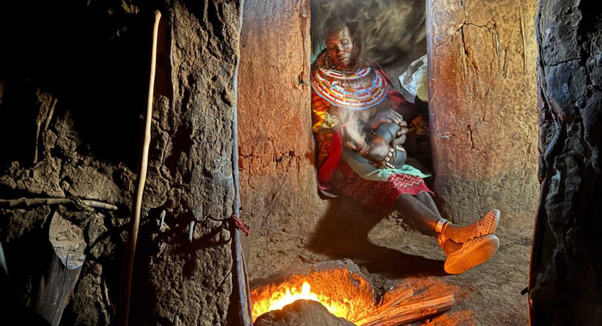 Woman warming herself by a fire in Kenya tribal house