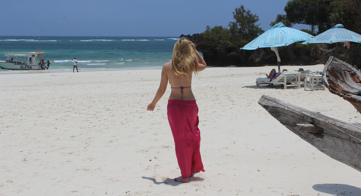 Teenager in pink sarong walking along Kenya beach