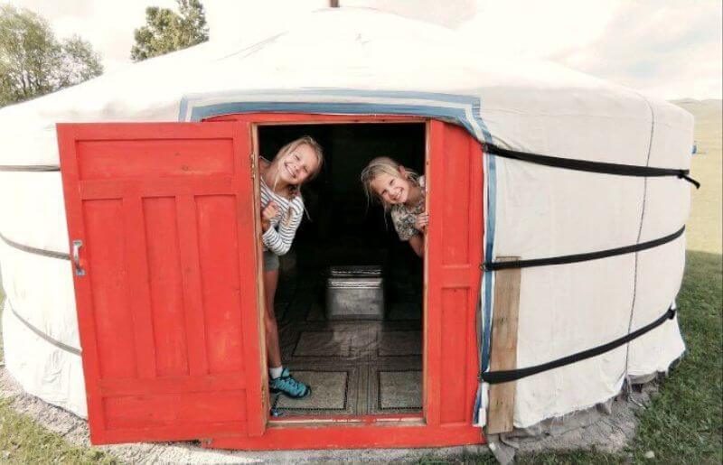 Fun places to stay on kids holidays abroad - teo girls peeping around the door of a yurt in Mongolia