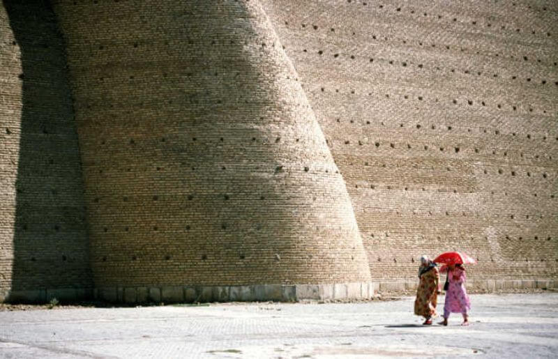 Woman walking past the ancient, vast fortified walls of Bukhara's Old Ark Fortress