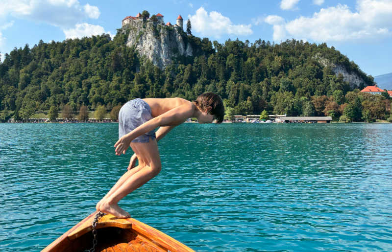 Go swimming in Lake Bled on a Europe family holiday, it's warm summer weather here as a boy dives off a boat into the lake