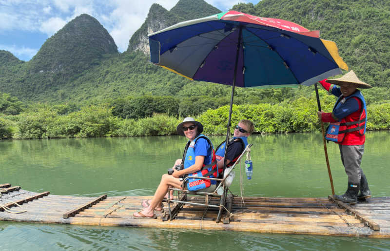 Family on rafting in Yangshuo River, China, shaded by a huge umbrella