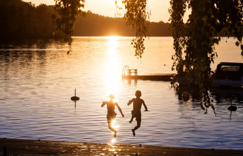 Two boys jumping into the lake at sunset - Sweden family holidays