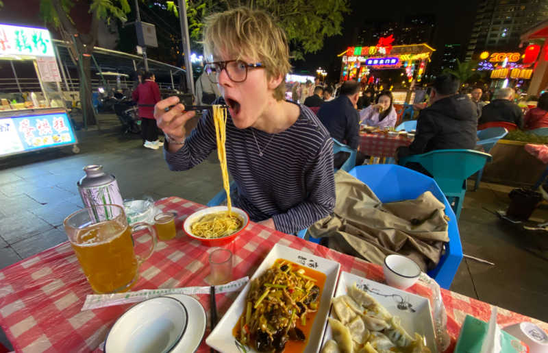 Young adult eating noodles al fresco on a family trip to China