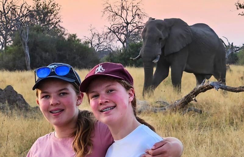 Two young girls stand in front of an elephant in Botswana