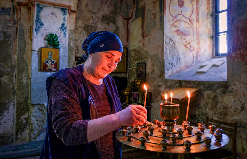 Georgia, woman lighting a candle inside Gelati Monastery, visit on family holiday to Georgia