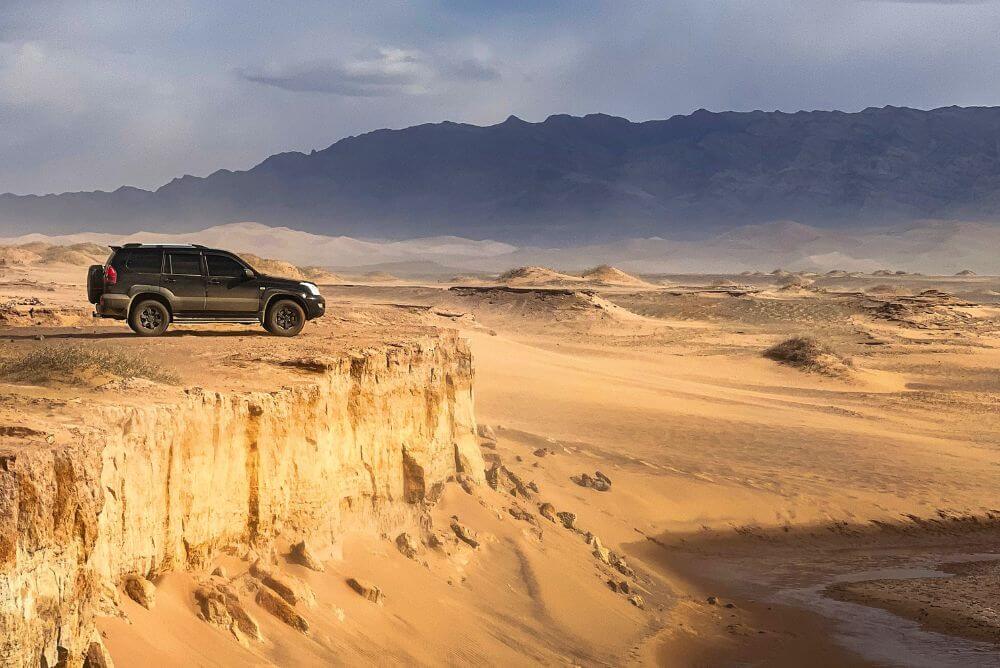 A jeep parked at the top of a cliff overlooking the Khongoryn Els sand dunes